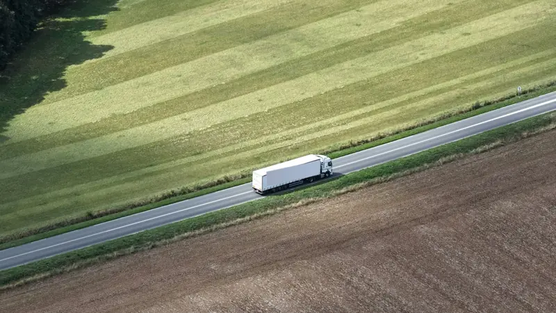 Camión en una ruta entre campos, visto desde arriba.